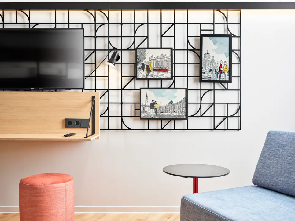 Wand vom Hotelzimmer mit einem Fernseher und einem kunstvoll gestalteten Gitter mit Bildern.
