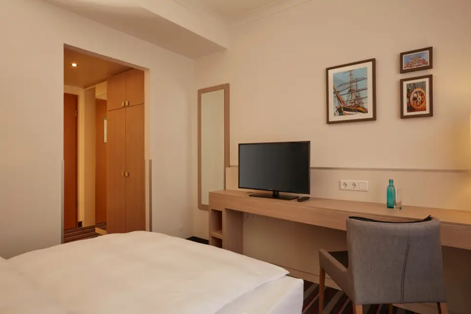 Einzelbett mit einem Schreibtisch am Fußende. Auf dem Schreibtisch steht ein Fernseher.