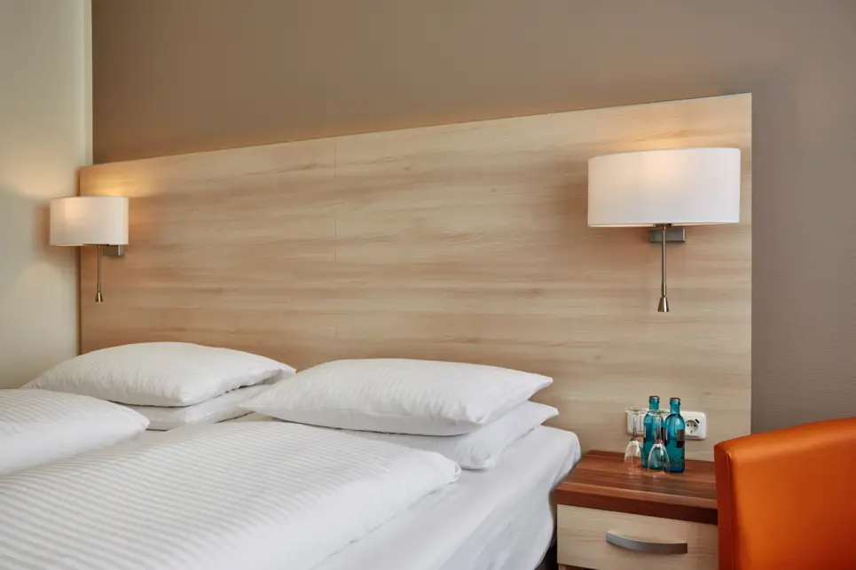 Nahaufnahme vom Doppelbett mit 2 Wasserflaschen und 2 Gläsern auf dem Nachttisch.