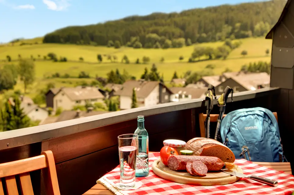 Balkon mit einem kleinen. gedeckten Tisch. Vom Balkon aus sieht man Wiesen und Wälder.