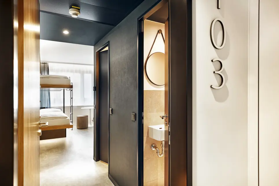 Blick in das Hotelzimmer vom Flur. Die Tür zum Badezimmer ist offen.