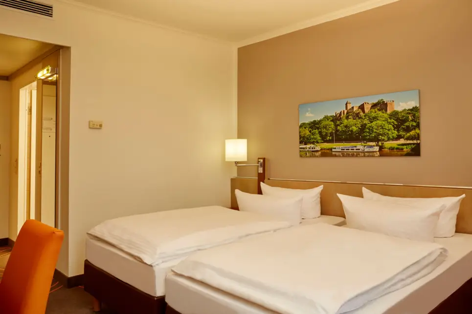 Twinbetten im Hotelzimmer mit eimer Lampe in der Ecke und einem Bild darüber.