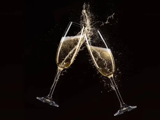 Zwei Sektgläser stoßen aneinander vor einem schwarzen Hintergrund.
