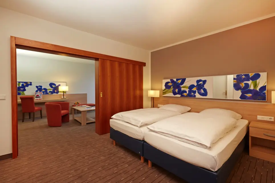 Schlafbereich mit einem Doppelbett. Durch eine Schiebetür sieht man den Wohnbereich.