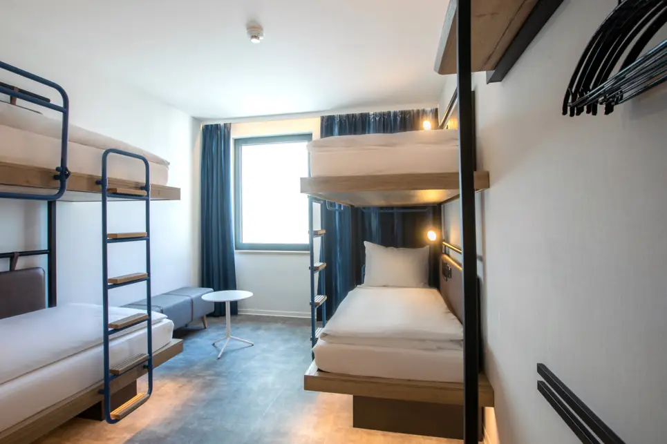 Inirekt beleuchtete Etagenbetten. Am Fenster ist eine kleine Sitzbank.