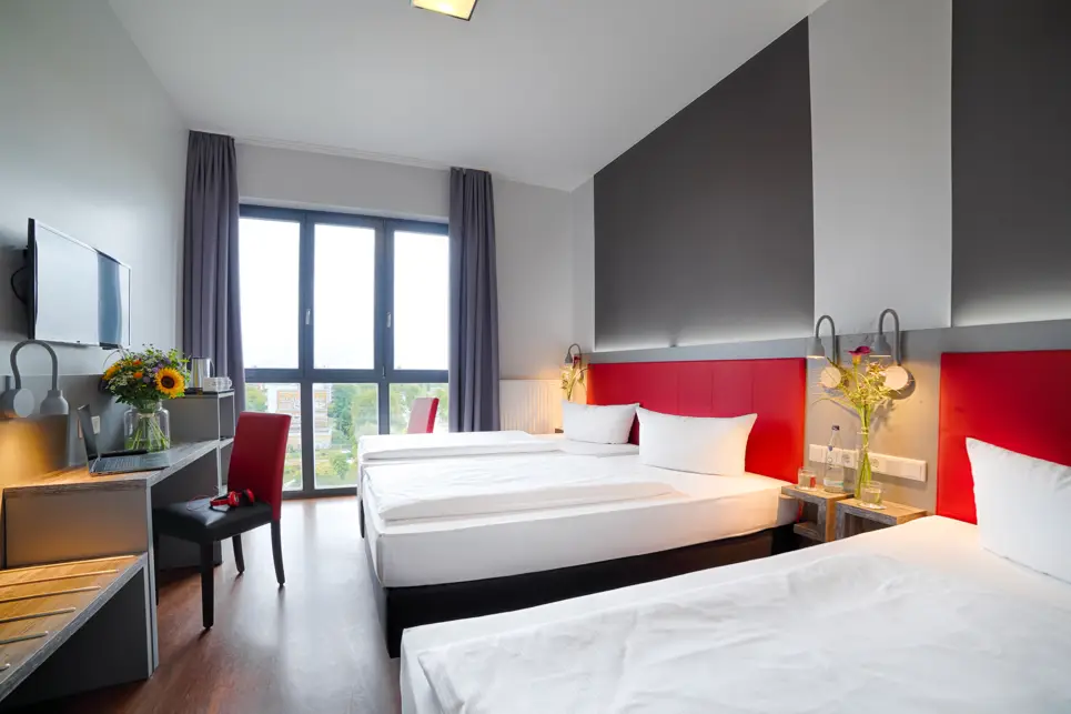 Drei Einzelbetten nebeneinander im Hotelzimmer. Vor den Betten steht ein Schreibtisch mit einem Stuhl.